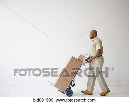 Stock Photo - African American deliveryman pushing hand truck with boxes. Fotosearch