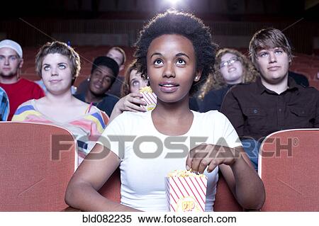 Stock Photography - African woman eating popcorn in movie theater. Fotosearch