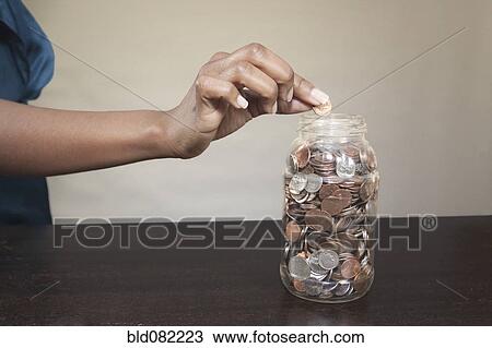 Stock Image - Black woman putting coin into jar. Fotosearch