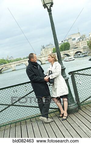 Stock Image - Caucasian couple holding hands on bridge. Fotosearch
