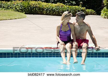 Stock Photo - Caucasian couple sitting near swimming pool. Fotosearch