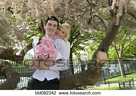 Stock Image - Caucasian couple with flowers kissing in park. Fotosearch
