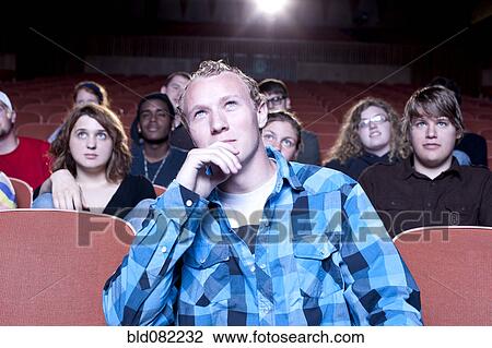 Stock Image - Caucasian man watching movie in theater. Fotosearch