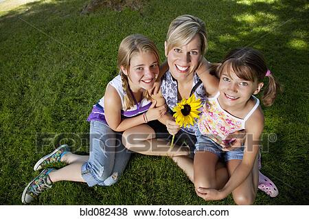 Stock Photo - Caucasian mother and daughters sitting grass. Fotosearch