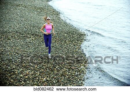 Stock Image - Caucasian woman running on pebble beach. Fotosearch