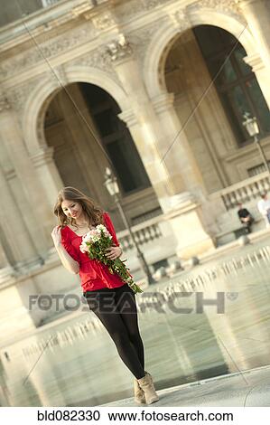 Stock Image - Caucasian woman standing near fountain with bouquet at the Louvre. Fotosearch