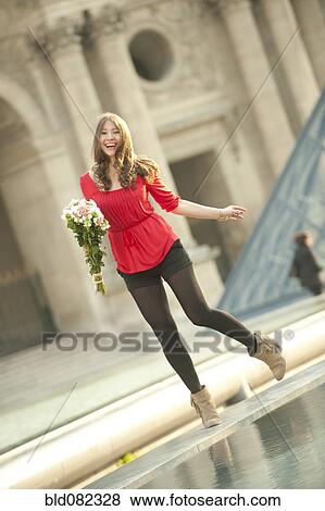 Stock Photo - Caucasian woman standing near fountain with bouquet at the Louvre. Fotosearch