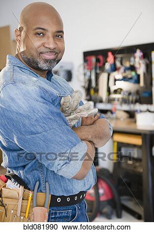 Stock Image - Construction worker in workshop with arms crossed. Fotosearch