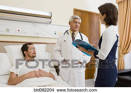 Picture - Doctor and nurse talking with patient in hospital room. Fotosearch