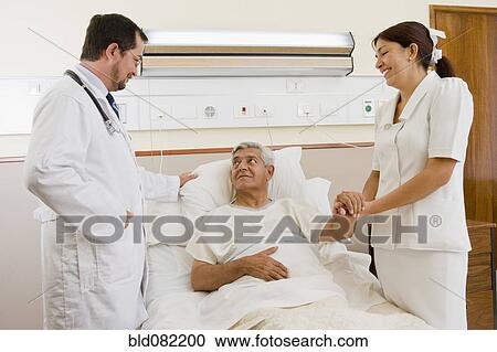 Stock Image - Doctor and nurse talking with patient in hospital room. Fotosearch
