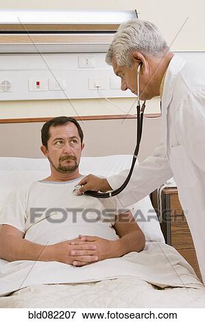 Doctor listening to patient's breathing in hospital room View Large Photo Image Stock Photo - Doctor listening to patient's breathing in hospital room. Fotosearch