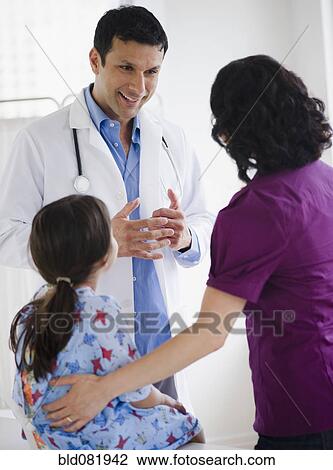 Stock Image - Doctor talking to mother and daughter in examination room. Fotosearch