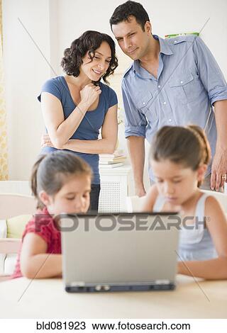Stock Image - Father and mother watching children using internet together. Fotosearch