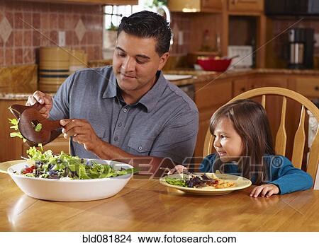 Picture - Father serving daughter salad at dinner table. Fotosearch