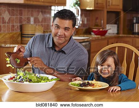 Stock Image - Father serving daughter salad. Fotosearch