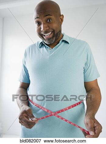 Stock Photo - Happy African American man measuring his waistline. Fotosearch