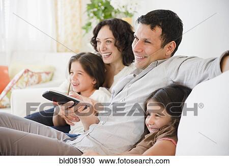 Stock Image - Happy family sitting on sofa watching television. Fotosearch