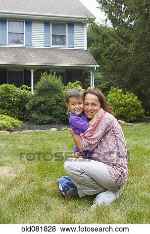Stock Photo - Hispanic mother hugging son in front yard. Fotosearch