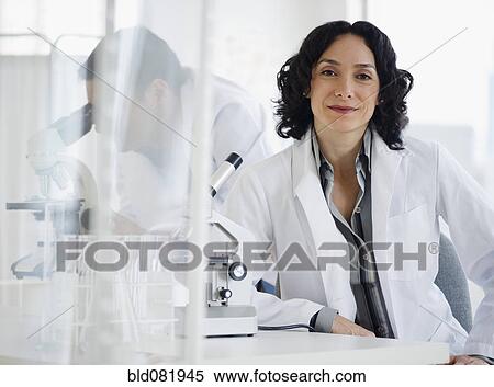 Stock Photography - Hispanic researcher in laboratory next to microscope. Fotosearch