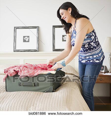 Stock Photograph - Hispanic woman in bedroom packing suitcase for trip. Fotosearch