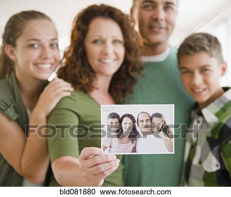 Stock Image - Hispanic woman with family holding out family portrait. Fotosearch