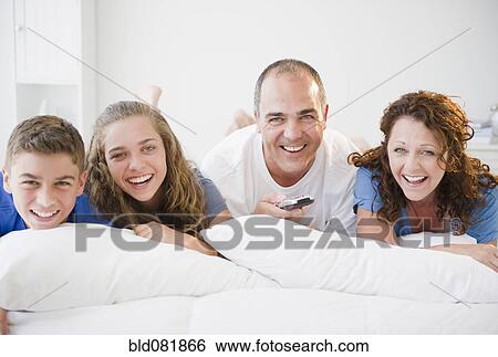 Stock Photograph - Laughing Hispanic family laying on bed together. Fotosearch