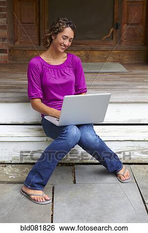 Stock Photograph - Mixed race woman sitting on step using laptop. Fotosearch