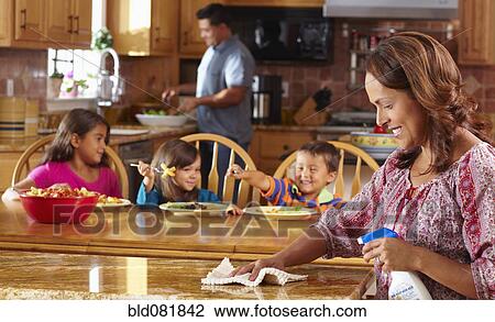 Stock Image - Mother cleaning while children eat in background. Fotosearch