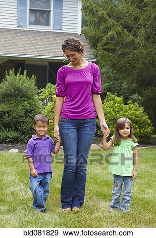 Stock Photo - Mother holding hands with son and daughter in front yard. Fotosearch
