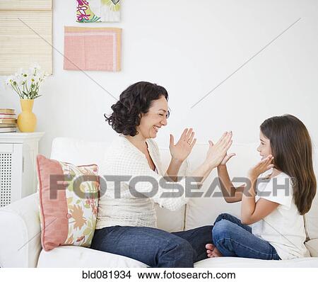 Picture - Mother playing hand game with daughter on sofa. Fotosearch