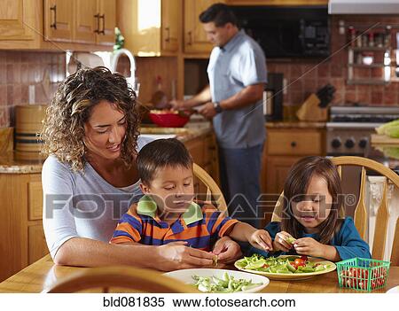Stock Photography - Mother, son and daughter shelling peas at dining table. Fotosearch