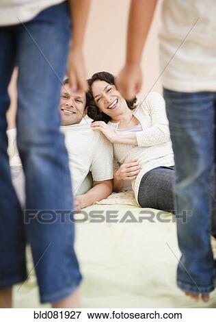 Stock Photo - Parents watching daughters jumping on bed. Fotosearch
