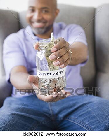 Stock Image - Smiling African American man holding out jar with retirement money. Fotosearch