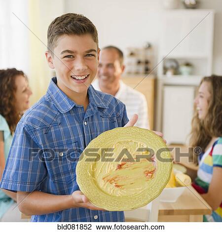 Smiling boy displaying empty plate with family at table in background View Large Photo Image Stock Image - Smiling boy displaying empty plate with family at table in background. Fotosearch