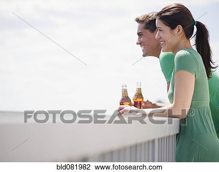 Smiling couple drinking beer on balcony View Large Photo Image Stock Image - Smiling couple drinking beer on balcony. Fotosearch