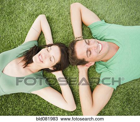 Stock Image - Smiling couple laying in grass together. Fotosearch