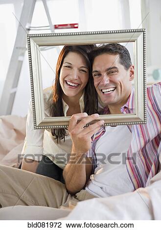 Stock Image - Smiling couple looking through empty frame. Fotosearch