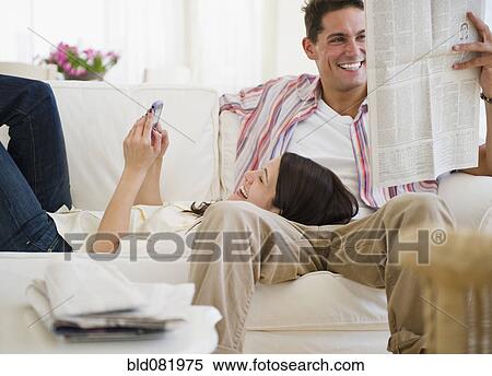 Smiling couple relaxing on sofa together with cell phone and newspaper View Large Photo Image Stock Photography - Smiling couple relaxing on sofa together with cell phone and newspaper. Fotosearch