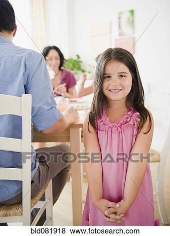 Stock Photo - Smiling girl with family at dinner table behind her. Fotosearch