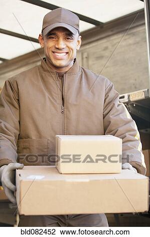 Stock Image - Smiling Hispanic delivery man carrying cardboard boxes. Fotosearch