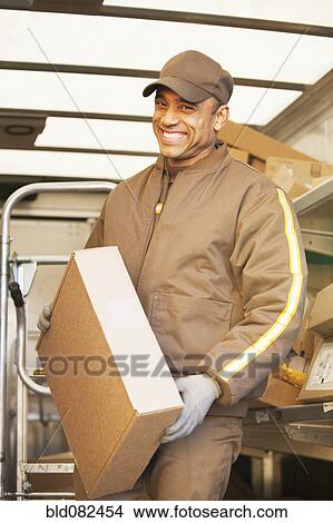 Picture - Smiling Hispanic delivery man holding cardboard box. Fotosearch