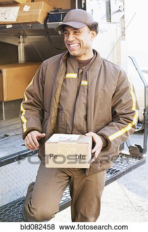 Smiling Hispanic delivery man holding cardboard box View Large Photo Image Stock Photo - Smiling Hispanic delivery man holding cardboard box. Fotosearch