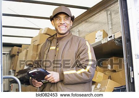 Stock Image - Smiling Hispanic delivery man standing in back of truck. Fotosearch