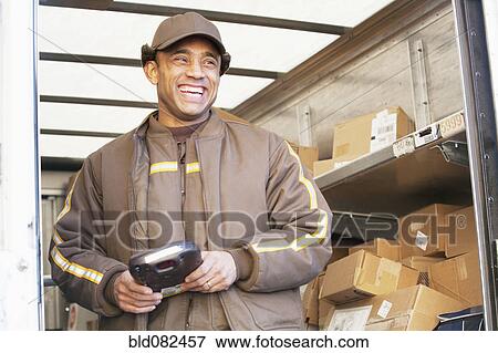 Stock Photo - Smiling Hispanic delivery man standing in back of truck. Fotosearch
