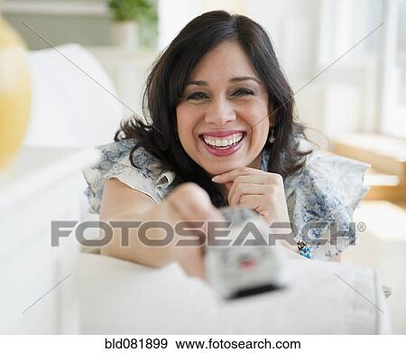 Smiling Hispanic woman changing channel with remote control View Large Photo Image Stock Photo - Smiling Hispanic woman changing channel with remote control. Fotosearch
