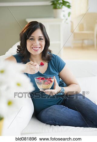 Smiling Hispanic woman eating cereal on sofa View Large Photo Image Stock Photograph - Smiling Hispanic woman eating cereal on sofa. Fotosearch
