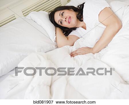 Stock Photo - Smiling Hispanic woman laying in bed. Fotosearch