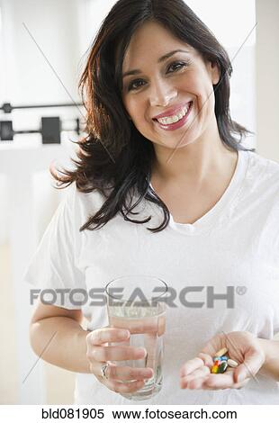 Stock Photography - Smiling Hispanic woman taking vitamins. Fotosearch