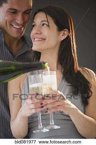 Stock Photo - Smiling man pouring Champagne for girlfriend. Fotosearch