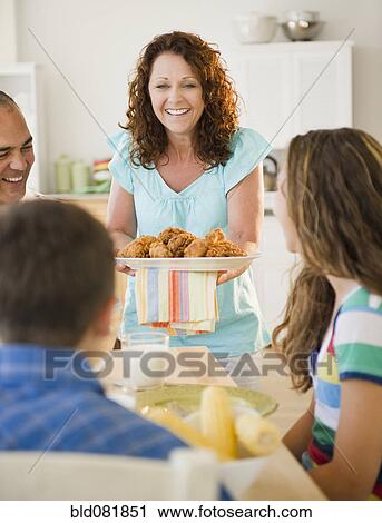Stock Image - Smiling woman serving family dinner. Fotosearch